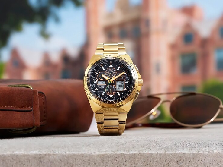 Citizen Promaster Skyhawk A-T JY8144-50E gold-tone pilot watch displayed upright on a ledge beside a brown leather bag and sunglasses, with a blurred cityscape in the background.