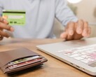 Person holding a bank card in front of a laptop, with a wallet on the desk