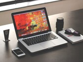 MacBook Pro on a dark desk next to a smartphone, glasses, and notebook