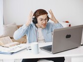 Man wearing headphones raising his hands in frustration in front of a laptop