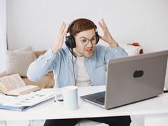 Man wearing headphones raising his hands in frustration in front of a laptop