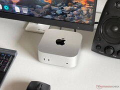 Apple M6 Mac mini on a desk in a gaming setup with a monitor, keyboard, mouse and speaker.