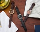 Three Citizen Rolan watches arranged on a wooden desk beside a notebook, pen, lamp, and open book, including the salmon-dial AW2110-14Z.