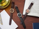 Three Citizen Rolan watches arranged on a wooden desk beside a notebook, pen, lamp, and open book, including the salmon-dial AW2110-14Z.