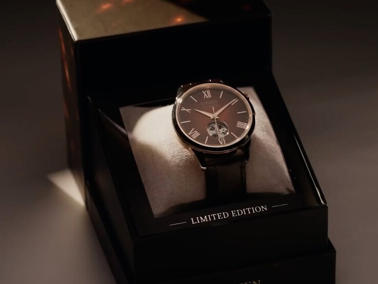 A wider, dramatically lit shot of the Citizen watch sitting on a cushion within its dark, tiered presentation box. A warm spotlight hits the watch face, and