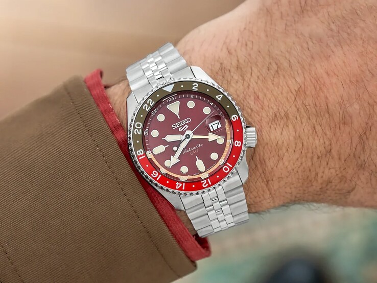 The Seiko 5 Sports GMT HDB016 worn on the wrist, showcasing its burgundy dial, two-tone red-and-brown GMT bezel, and stainless steel bracelet.