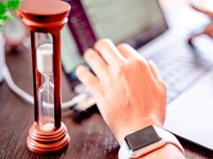 Hourglass next to a hand on a laptop keyboard