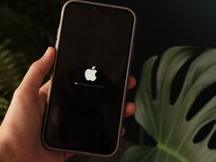 A hand holds an iPhone, the Apple logo and a progress bar are lit on the screen.