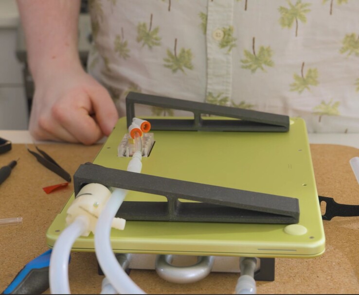 Modified MacBook Neo with external pump and tubing setup for DIY liquid cooling