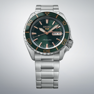 Seiko 5 Sports SKX HDB005 with a dark green dial, matching green bezel, rose gold-colored hands and indexes, and stainless steel bracelet shown against a light gray background.