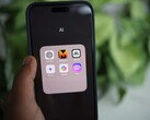 A hand holds a smartphone showing a folder named AI with apps including Gemini, ChatGPT and Claude