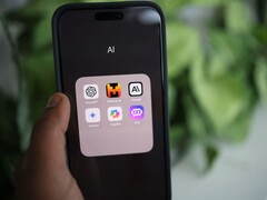 A hand holds a smartphone showing a folder named AI with apps including Gemini, ChatGPT and Claude