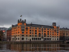 Orange Rosenbad building with a Swedish flag by the water in Stockholm under a cloudy sky