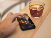 A hand enters a PIN on a smartphone lying next to a glass of tea on a wooden table