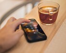 A hand enters a PIN on a smartphone lying next to a glass of tea on a wooden table