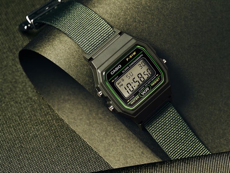 Casio F-91WF-3A digital watch with a green-accented black case and woven green fabric strap, photographed against a dark green textured background.
