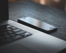 A smartphone lying next to an open laptop on a dark desk