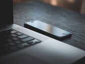 A smartphone lying next to an open laptop on a dark desk