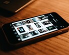 A smartphone lying on a wooden desk, its display showing a grid of photos