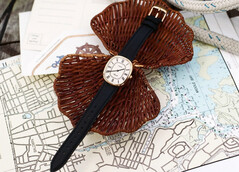 Gold-tone Noah × Timex Boatswain watch with white Roman numeral dial and black leather strap, photographed on nautical charts and woven wicker.