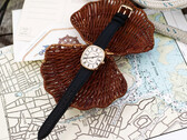 Gold-tone Noah × Timex Boatswain watch with white Roman numeral dial and black leather strap, photographed on nautical charts and woven wicker.