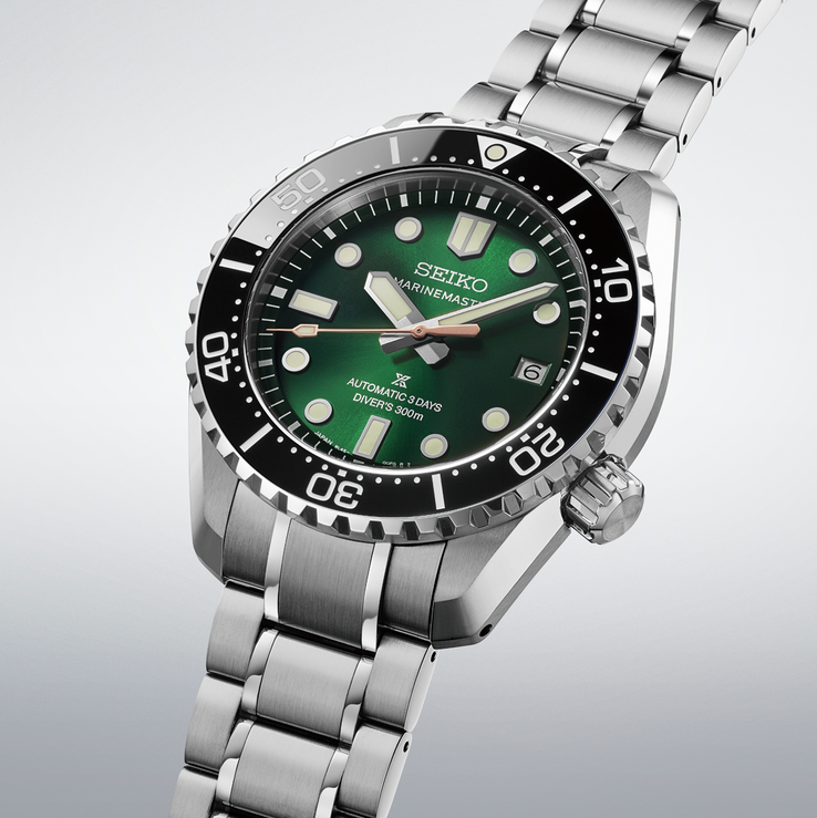 Detailed three-quarter view of the watch showing the textured green dial, pink-gold-colored seconds hand, oversized LumiBrite markers, black ceramic bezel, and stainless steel bracelet.