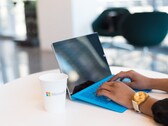 Hands typing on a laptop with a blue keyboard next to a cup with a Microsoft logo