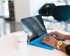 Hands typing on a laptop with a blue keyboard next to a cup with a Microsoft logo