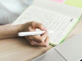 A person is writing notes in a notebook next to an open laptop