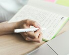 A person is writing notes in a notebook next to an open laptop