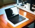 Matte black Razer Blade 16 gaming laptop open on a wooden desk displaying a high-contrast wallpaper, with a desk setup in the background.