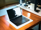 Matte black Razer Blade 16 gaming laptop open on a wooden desk displaying a high-contrast wallpaper, with a desk setup in the background.