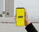 A hand holding a smartphone with the word eSIM large on a yellow screen.
