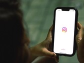 Woman holding a smartphone in both hands, the display shows the Instagram start screen