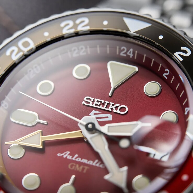 Close-up of the Seiko 5 Sports GMT HDB016’s maroon dial, featuring luminous geometric hour markers, broad hands, a gold-tone GMT hand, and a two-tone 24-hour bezel.