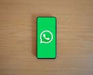 Smartphone on a wooden desk showing the green WhatsApp start screen with its logo.