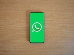 Smartphone on a wooden desk showing the green WhatsApp start screen with its logo.