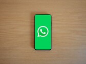 Smartphone on a wooden desk showing the green WhatsApp start screen with its logo.